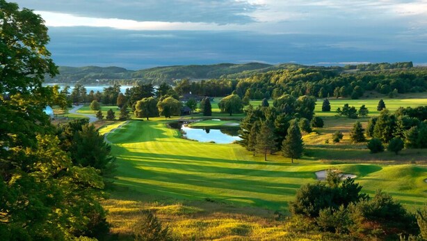 Ein Golfplatz mit Teich, umgeben von Bäumen und Hügeln.