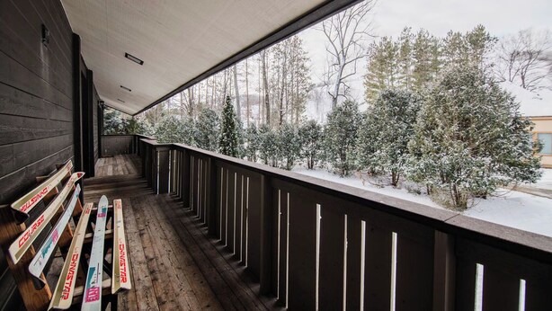 Eine Holzterrasse mit Bänken, Blick auf verschneite Bäume und ein Gebäude im Hintergrund.