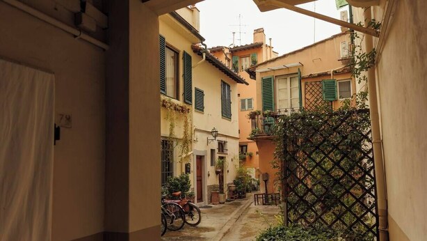 A narrow alleyway with buildings on either side, a bicycle, and a lattice fence. - Florence House San Zanobi (Firenze)