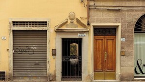 A building facade with a closed metal shutter, a wooden door with a brass handle, and a small sign above the door. - Florence House San Zanobi (Firenze)