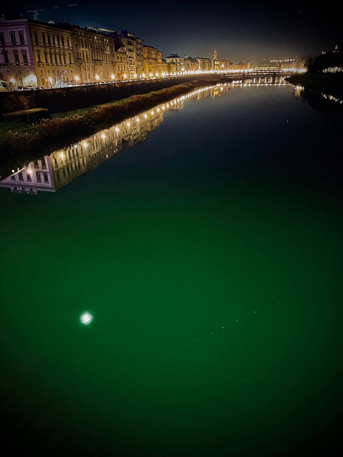 A nighttime view of a river with buildings on one side reflecting in the water.