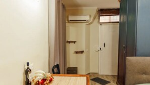 A room with a wooden table, a bottle, and a glass on it. There is a chair, a small stool, and a cabinet. An air conditioning unit is mounted on the wall. - Florence House San Zanobi (Firenze)