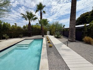 A swimming pool with a clear blue water surface, surrounded by a gravel path and various plants.