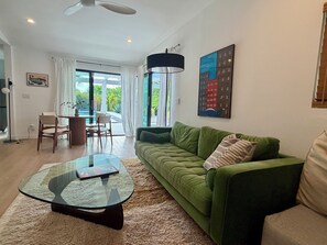 A modern living room with a green sofa, a glass coffee table, and a dining area with a table and chairs. - The Knot - The Ultimate Palm Springs Bungalow (Palm Springs)