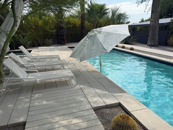 A poolside area with lounge chairs and a white umbrella.