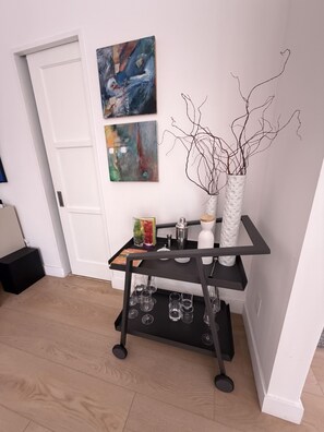 A room with a black metal cart holding glasses and a white vase with branches. There are abstract paintings on the wall. - The Knot - The Ultimate Palm Springs Bungalow (Palm Springs)