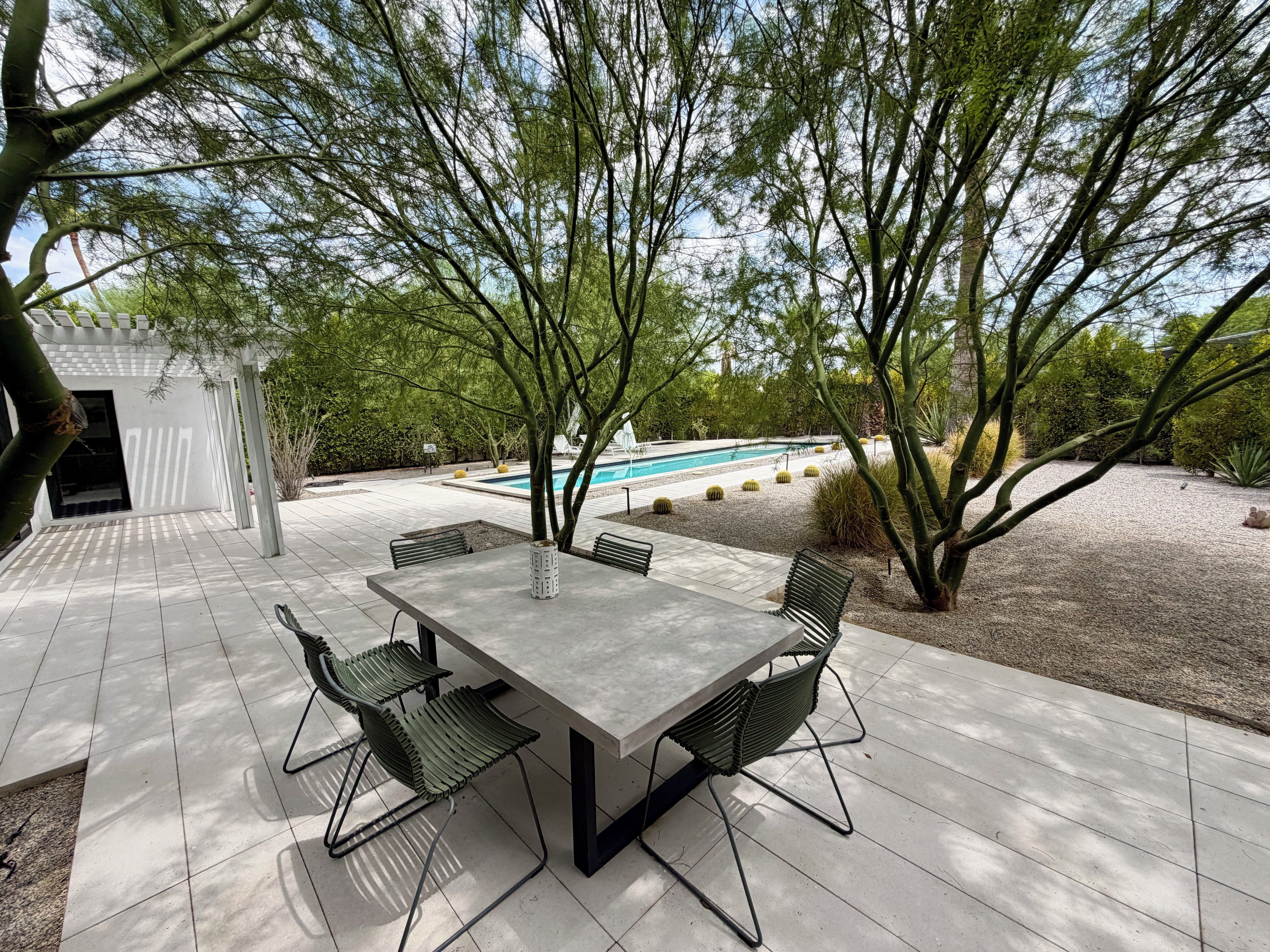 Une terrasse extérieure avec une table et des chaises, entourée d’arbres et bordée d’une piscine.
