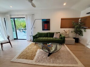 A modern living room with a green sofa, a glass coffee table, and a view through a glass door to an outdoor area. - The Knot - The Ultimate Palm Springs Bungalow (Palm Springs)