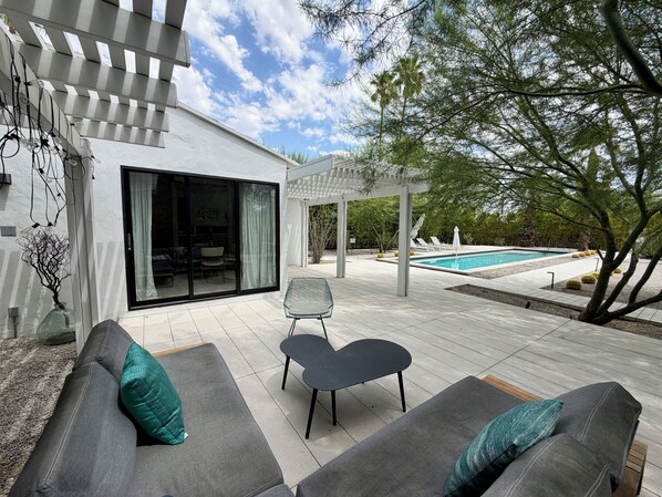 A modern outdoor patio with a pool, grey sofas, and a pergola.