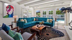 A spacious living room with a teal sectional sofa, a coffee table, and a large abstract painting on the wall.