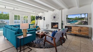 A spacious living room with a teal sofa, a wooden coffee table, and a TV displaying a pool view.