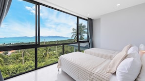 Ein Schlafzimmer mit großem Fenster und Blick auf eine tropische Landschaft und das Meer.