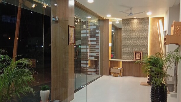 A modern lobby with glass doors, a ceiling fan, recessed lighting, and potted plants. - Hotel Kashni (Maihar)