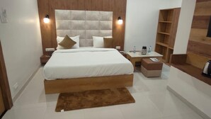 A modern bedroom with a large bed, wooden headboard, bedside tables, a nightstand, a coffee table, and a built-in shelf unit. - Hotel Kashni (Maihar)
