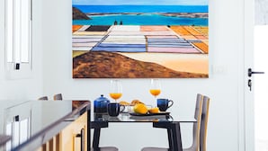 A dining table with breakfast items, a painting of a coastal scene, and a view of the sea.