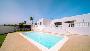 A rectangular swimming pool with a white border, surrounded by a paved patio area.