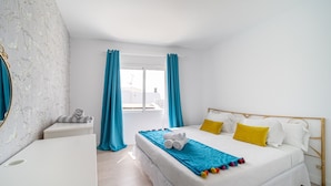 A bedroom with a bed, a bedside table, a mirror, and a window with curtains.