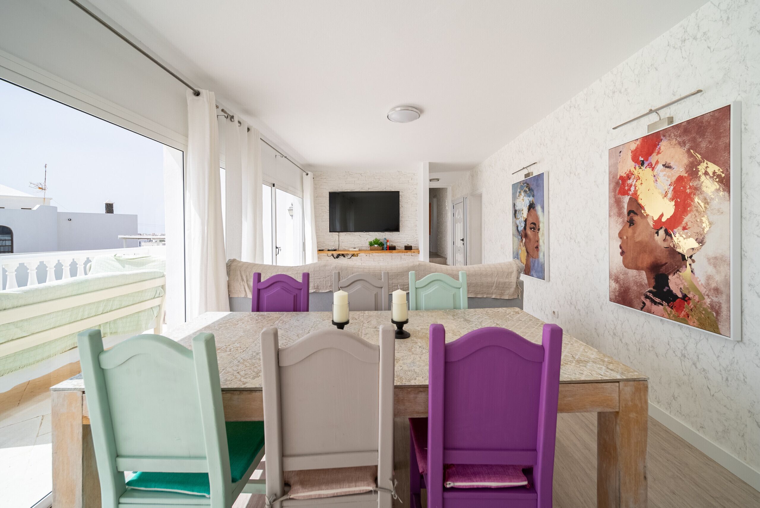 A modern dining area with a long table, colorful chairs, and a large painting on the wall.