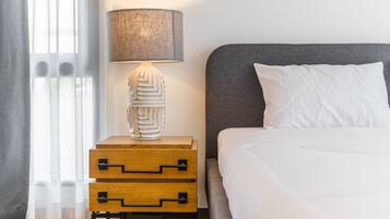 A neatly made bed with white bedding, a grey headboard, and a bedside lamp with a textured lampshade.