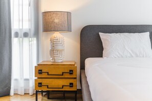 A neatly made bed with white bedding, a grey headboard, and a bedside lamp with a textured lampshade.