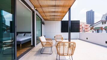 A modern balcony with a bed, two wicker chairs, and a view of the cityscape.