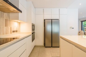 A modern kitchen with white cabinetry, a stainless steel refrigerator, and a built-in oven.