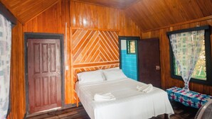 Una habitación de madera con una cama, una ventana con cortinas y una puerta.