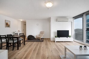 A modern living room with a dining area, a flat-screen TV, and a large window with a city view.