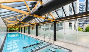 An indoor swimming pool with glass walls, a clear ceiling, and a modern architectural design.
