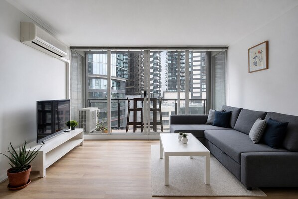 A modern living room with a sofa, TV, and a balcony with a city view.