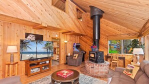 Un intérieur de chalet chaleureux, avec un revêtement mural en bois, une cheminée, un téléviseur et un canapé.