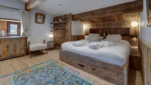 A cozy bedroom with a wooden headboard, a bed with neatly folded towels, a small bedside table with a lamp, and a chair. - Ski-in/ski-out chalet with pool and sauna in Val-d'Isère (Val-d'Isère)