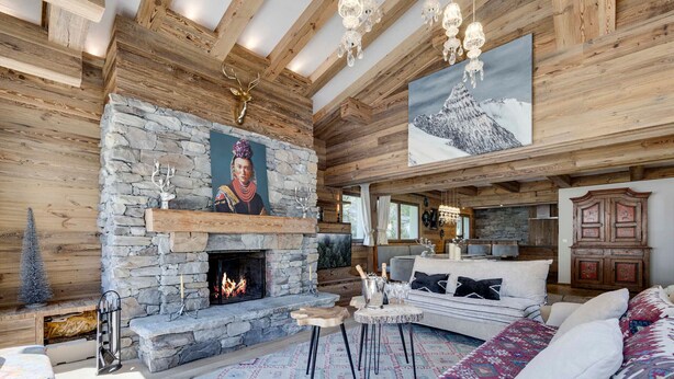 A cozy log cabin interior with a stone fireplace, wooden beams, a large sofa, and a chandelier. - Ski-in/ski-out chalet with pool and sauna in Val-d'Isère (Val-d'Isère)