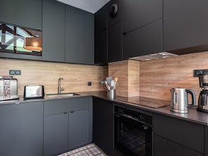 Une cuisine moderne avec des meubles de couleur sombre, un pare-feu en bois, un grille-pain, une machine à café et un lave-vaisselle.