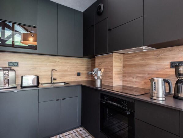 A modern kitchen with dark cabinets, a wooden backsplash, a toaster, a coffee maker, and a dishwasher.