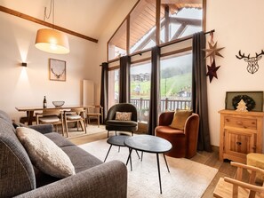 A spacious living room with a high ceiling, large windows, and a view of a green landscape.