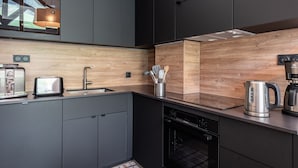 A modern kitchen with dark cabinets, a wooden backsplash, a toaster, a coffee maker, and a dishwasher. - Renovated duplex in center with parking and wifi (La Plagne Montalbert)