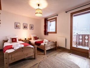 Quarto de hotel com duas camas de madeira, uma janela ampla com vista, uma luminária no teto e um radiador.