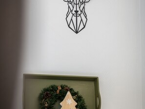 A wall with a geometric deer head decoration and a wooden Christmas tree with a wreath below it.