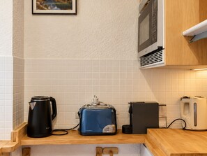 A kitchen with a coffee maker, toaster, and kettle on a wooden countertop. - Renovated ski-in studio with balcony and Wi-Fi (Méribel)