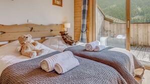 A bedroom with two beds, a wooden headboard, a large window, and a view of a forest.