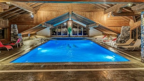 An indoor swimming pool with a wooden ceiling and stone walls, surrounded by lounge chairs.