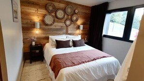 Un dormitorio con pared de madera, una cama con ropa blanca, un plaid marrón y platos decorativos sobre la cama.