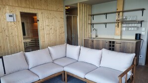 Una sala moderna con un sofá seccional, una mesa de centro de madera y una cocina con estantes y un lavamanos.