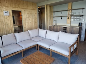 Una sala moderna con un sofá seccional, una mesa de centro de madera y una cocina con estantes y un lavamanos.