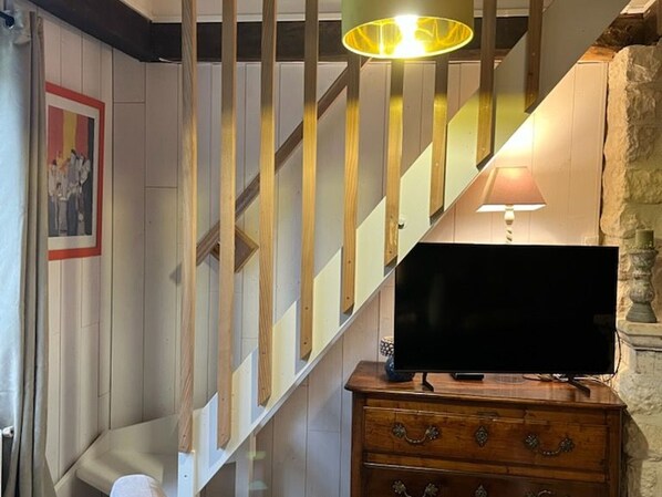 A staircase with wooden balusters and a modern light fixture, a flat-screen TV on a wooden dresser, and a stone wall.