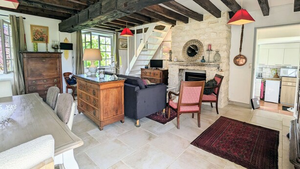 A rustic living room with exposed wooden beams, a fireplace, and a kitchen visible through an open door. - Peaceful Berry retreat with garden and fireplace (Brives)
