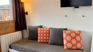 A small, cozy room with a bed, a TV mounted on the wall, and a window with curtains. - Comfortable 2-room apartment with panoramic view in Avoriaz (Avoriaz)