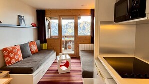 A modern room with a sofa, a small table, and a kitchen area including a microwave and stove. - Comfortable 2-room apartment with panoramic view in Avoriaz (Avoriaz)