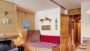 Ein gemütliches Zimmer mit einer Holzsofa, einem kleinen Tisch mit einer Lampe, einem Kamin und einem Essbereich mit Tisch für zwei Personen.